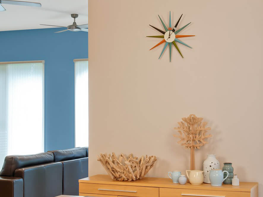 Neutral dining room with blue feature wall timber cabinet brown lounge and colourful clock 